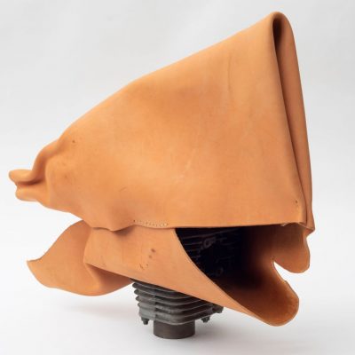 Folded and layered tan leather forming a rectangle shape held off the ground by a protruding cylindrical motorcycle part