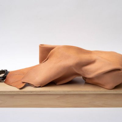 Smooth, tan leather folded and molded in an abstract shape with part of a car engine piston extending from a fold