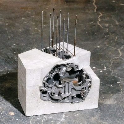 A cube shaped piece of concrete with engine parts embedded and exposed so that their internal workings are visible