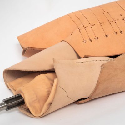 Tan leather, molded in an abstract shape with stitching, drawn electrical diagrams and a part of a motorcycle engine extending from it